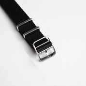 Close-up of the Herringbone Twill in Artillery Black watch band from RSM Watch Strap, with a polished silver buckle and loops.