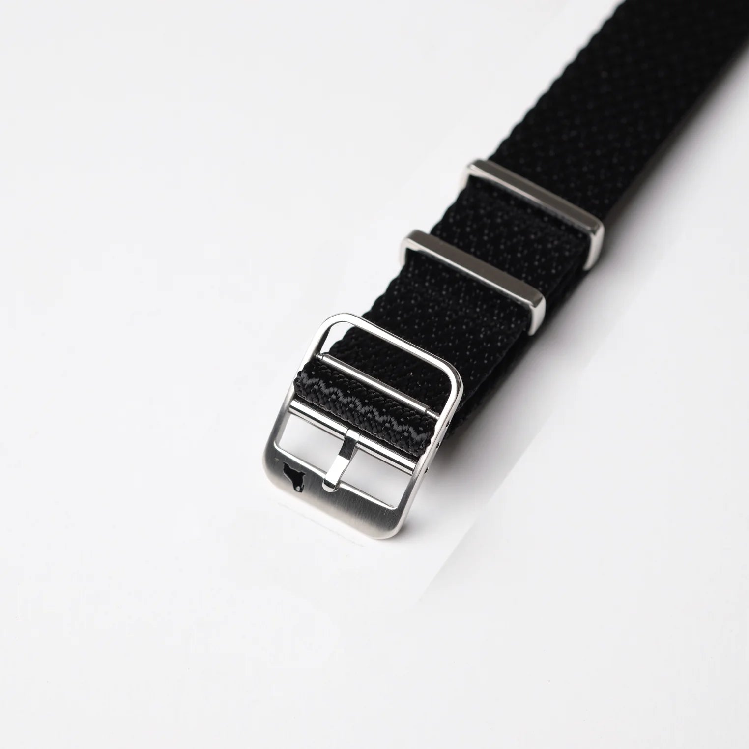 Close-up of the Herringbone Twill in Artillery Black NATO watch band by RSM Watch Strap, with a silver buckle and two loops on a white background.