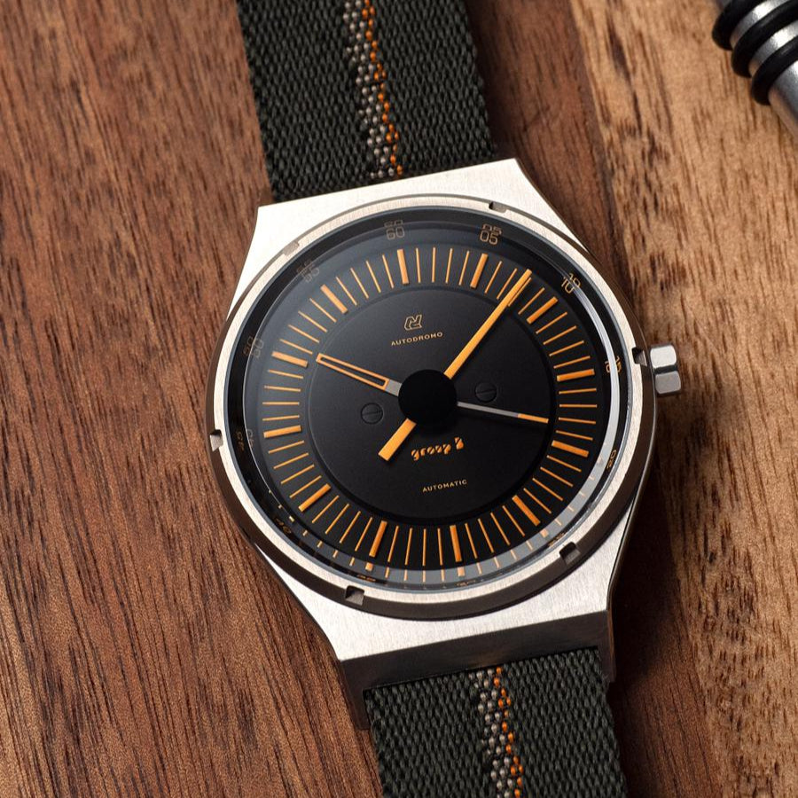 Autodromo watch with 70s-style orange markers and hands pairs with RSM’s dark green single-pass engraved stripe watch strap featuring an orange stripe.