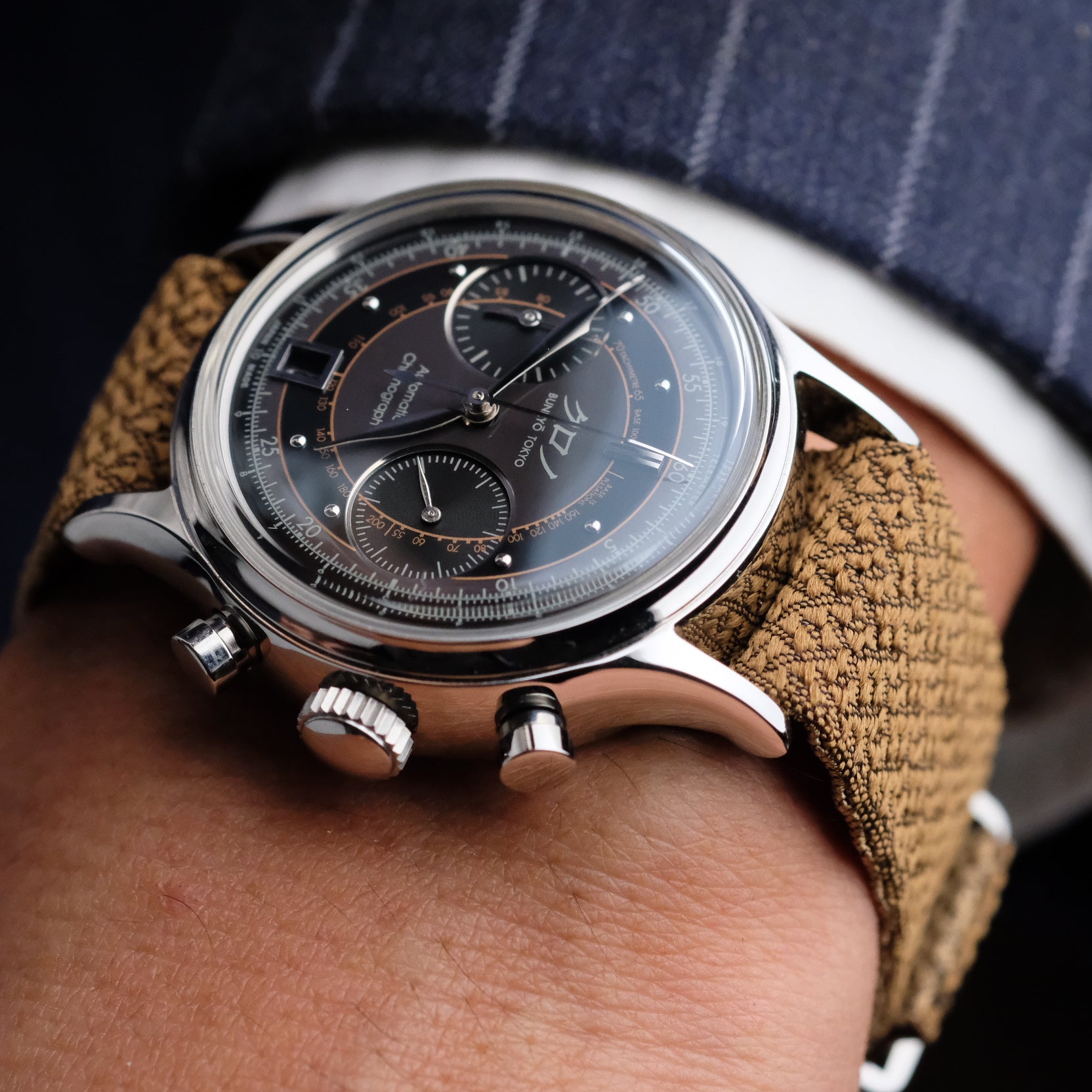 A man in a suit wears a watch with a Bronze Reversible Silk Single Pass RSM Watch Strap, showcasing sophistication and style.