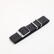 Single Pass X-Hatch Watch Strap in Black, textured polyester with metallic buckles and adjustment holes, lies flat on a white surface, featuring checkered patterns.