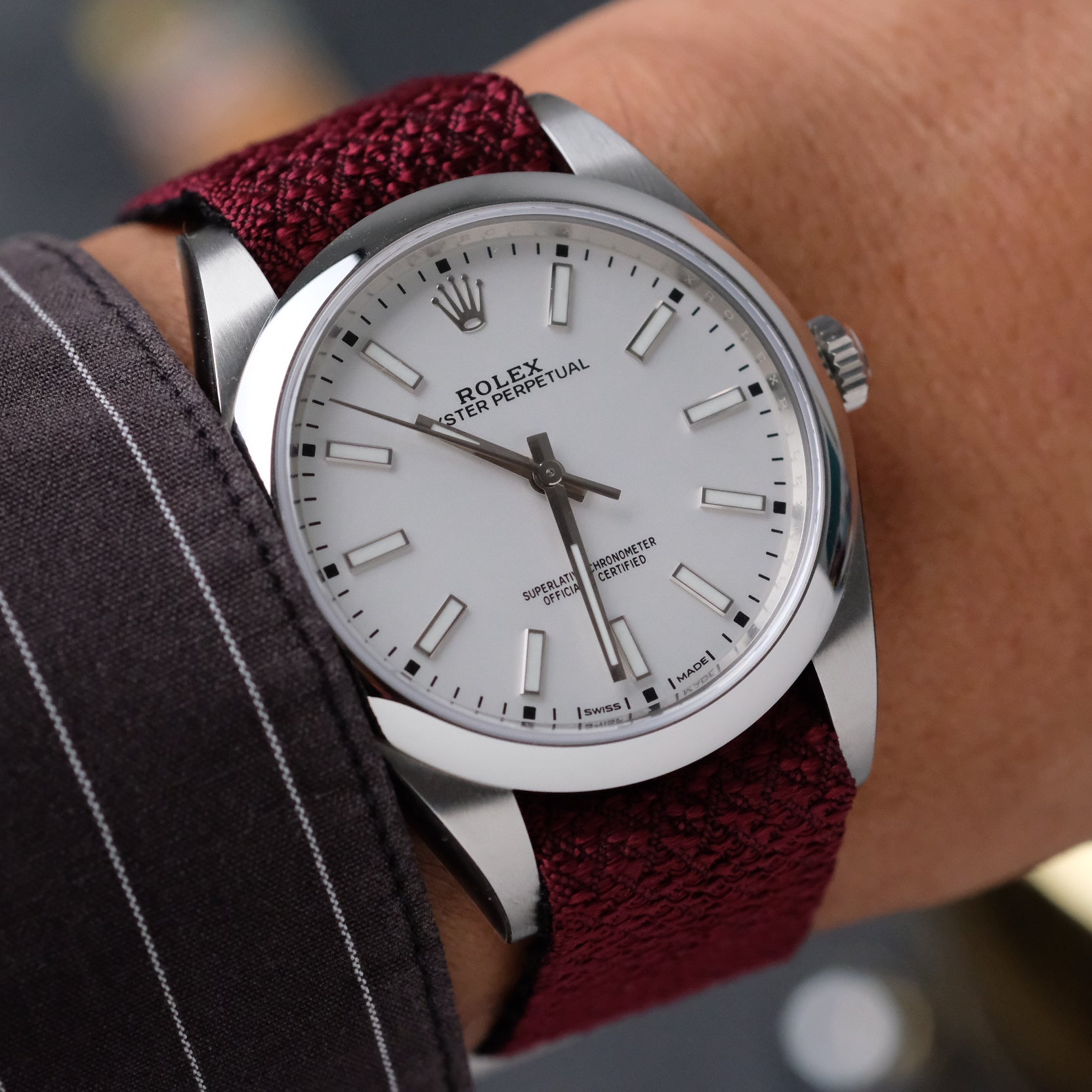 A Rolex with a burgundy Reversible Silk Single Pass RSM Watch Strap is worn on a man’s wrist, complementing his shirt.