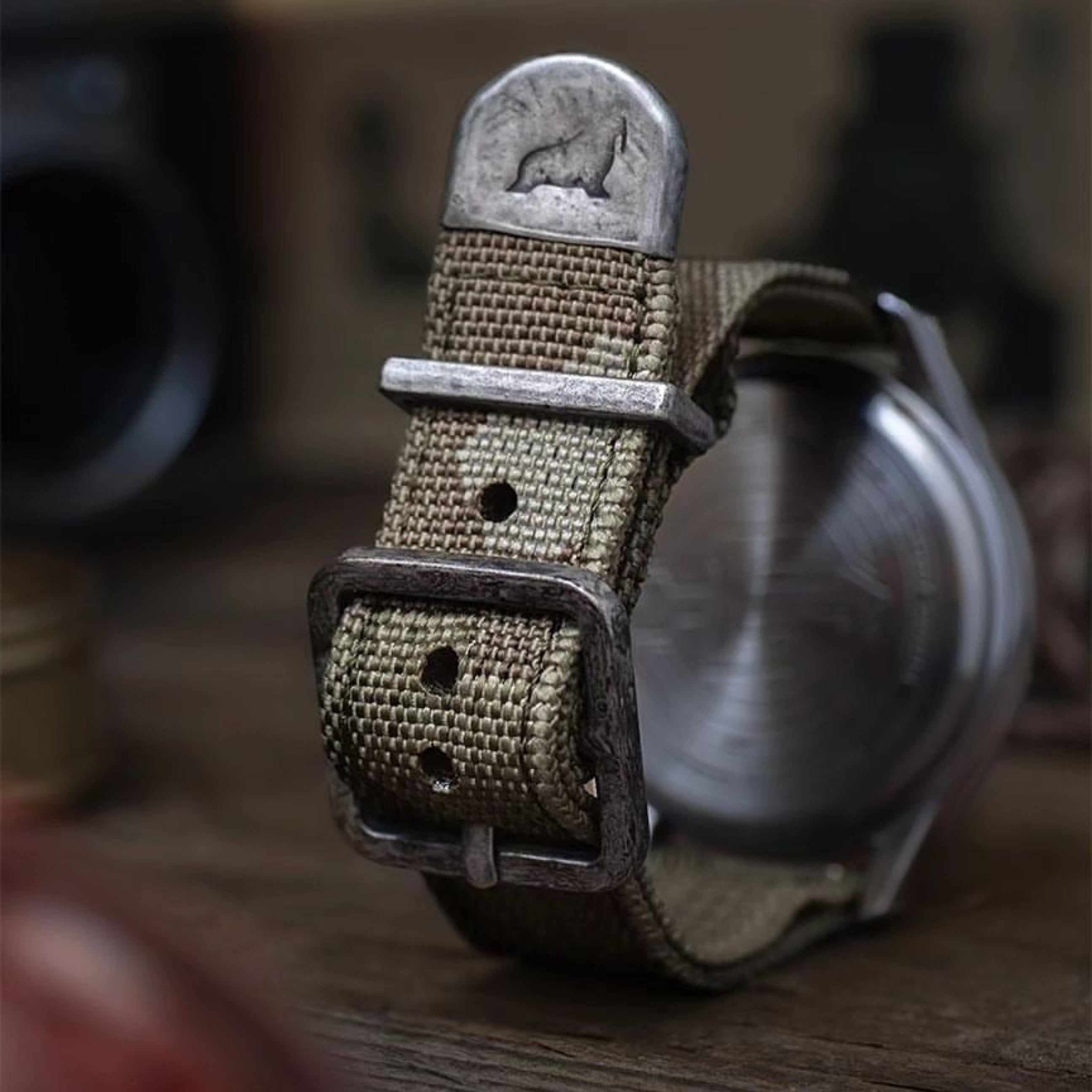 The RSM camo 2-piece strap is mounted on a watch, showcasing detailed yarns woven in a camo pattern with rugged, distressed silver hardware. Photo by Timex.VintageMX