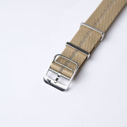 Close-up of the Engraved Stripe beige nylon watch strap with adjustable length, silver buckle, metal loops, jacquard weave, and fine stitching.