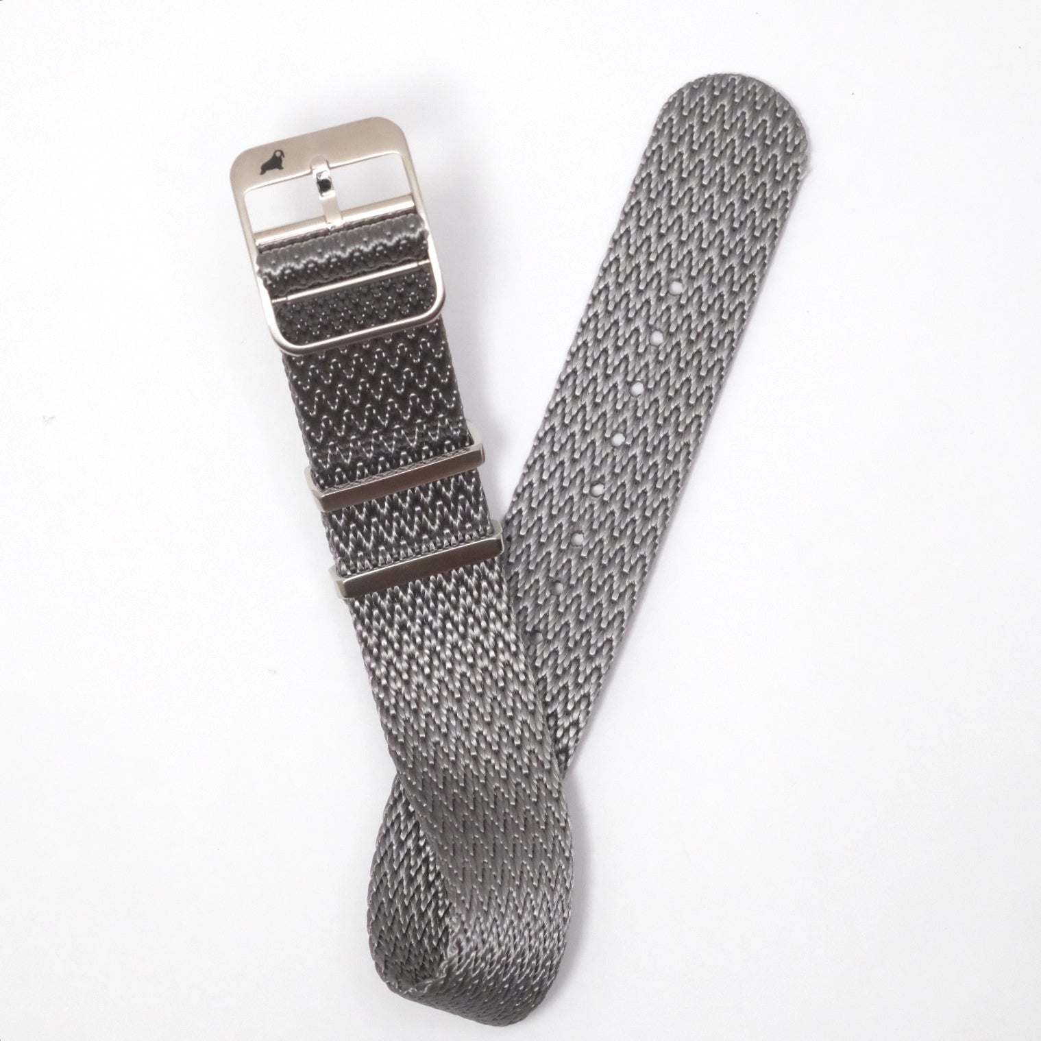 The Herringbone Twill in Field Gray band by RSM Watch Strap, with a metallic buckle, lies partially rolled on a white surface.