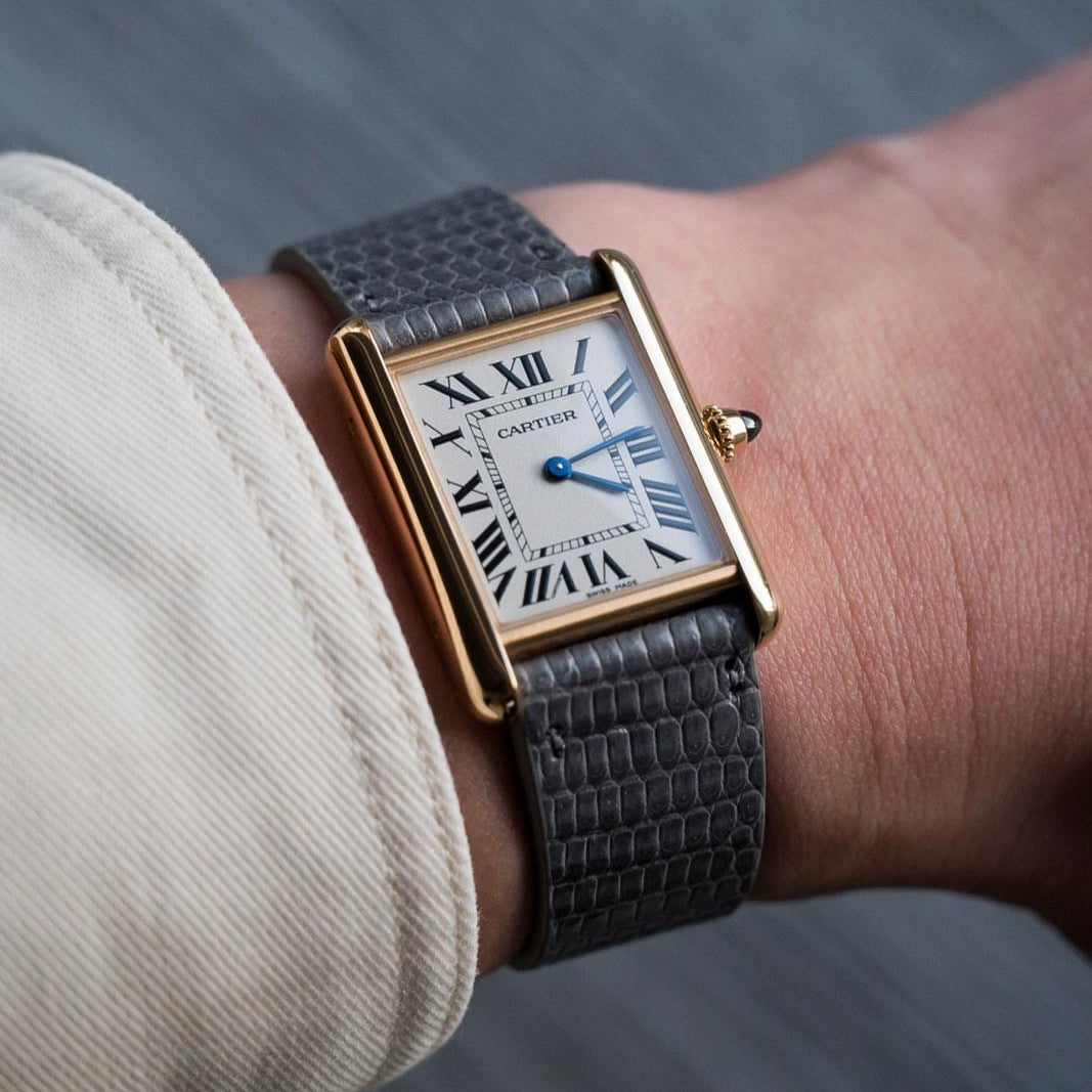 Wrist shot of Cartier Tank gold case, white dial, black Roman markers, blue steel hands, worn with lizard strap by RSM.