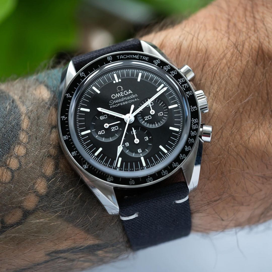 Tattooed arm wearing Omega Speedmaster paired with RSM's Black Coal Fine Canvas watch strap, featuring white stitching details. Photo by Hands and Bezel