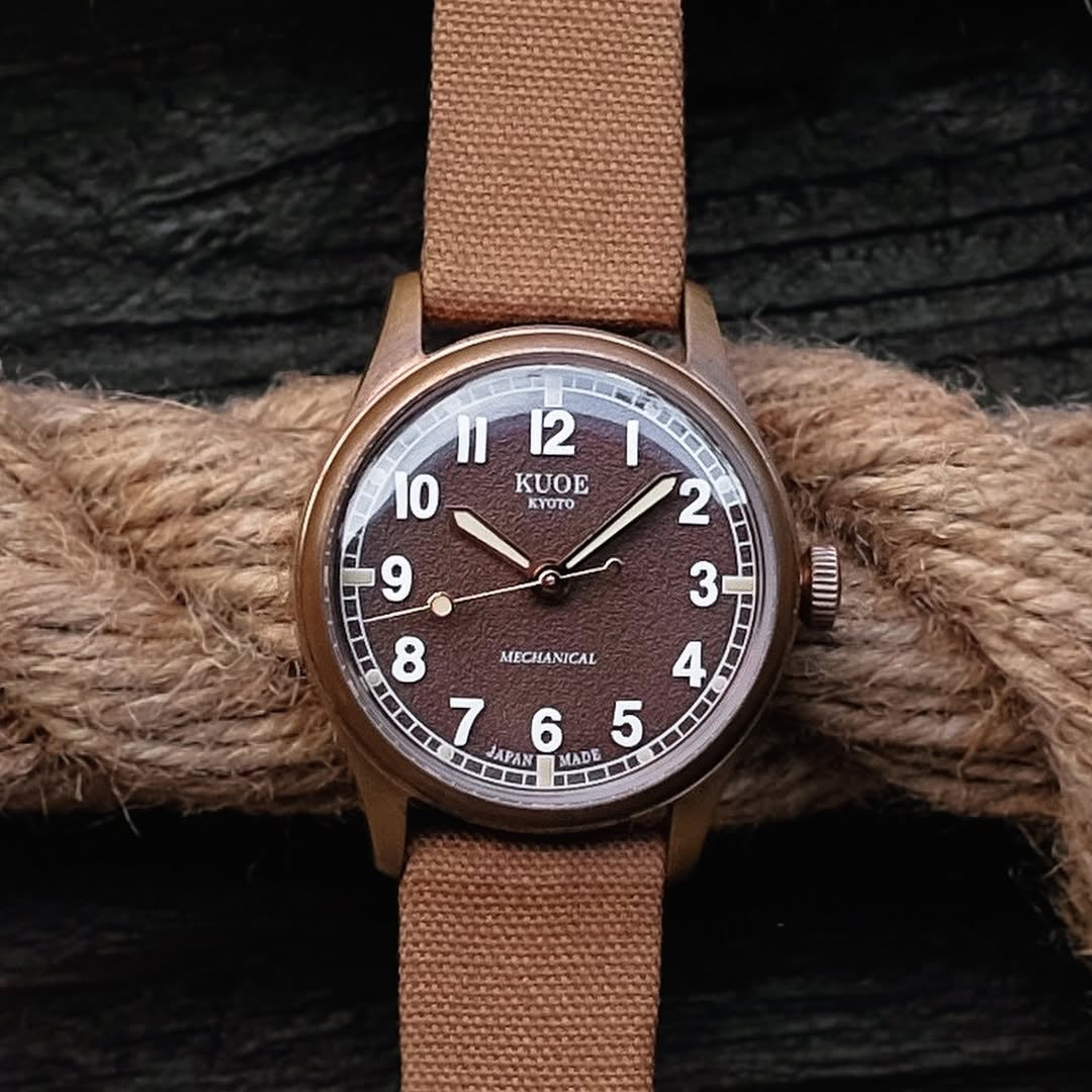 Kuoe Old Smith bronze case with brown dial, paired with RSM's Fine Canvas strap in Basic Roast Tea color. Set against rope and black timber grain.