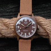 Kuoe Old Smith bronze case with brown dial, paired with RSM's Fine Canvas strap in Basic Roast Tea color. Set against rope and black timber grain.