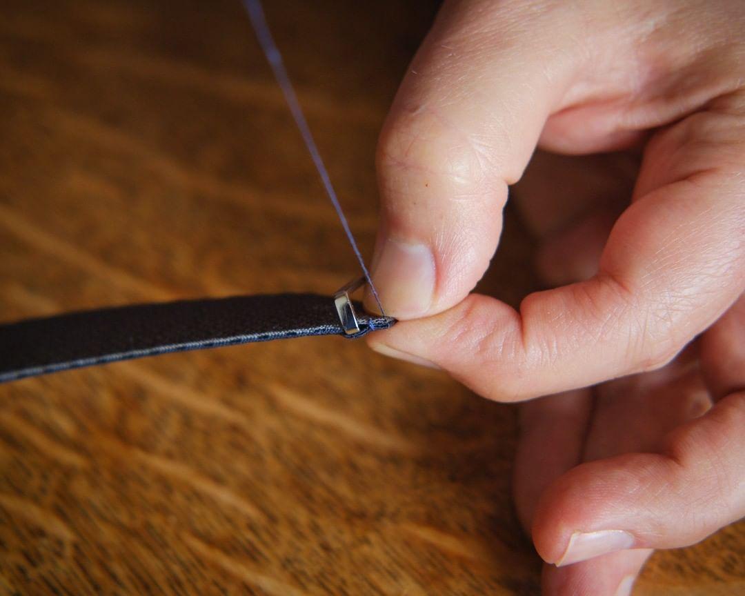 A man sewing thread to add a perfect finishing touch to a blue watch strap by RSM, showcasing skilled craftsmanship and attention to detail.