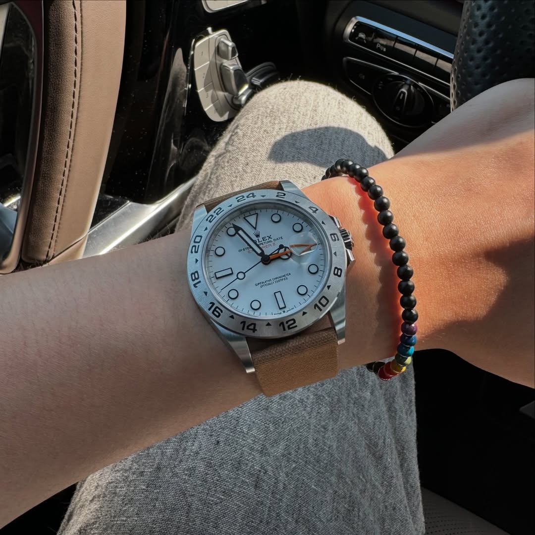 Rolex Explorer 2 Polar on the wrist with RSM's Fine Canvas Strap in Roasted Tea, black beads, resting on the steering wheel in a car interior.