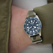 The Tudor FXD blue is seen on a wrist with the RSM camo strap. The 316L keeper showing with the wearer with olive jacket.