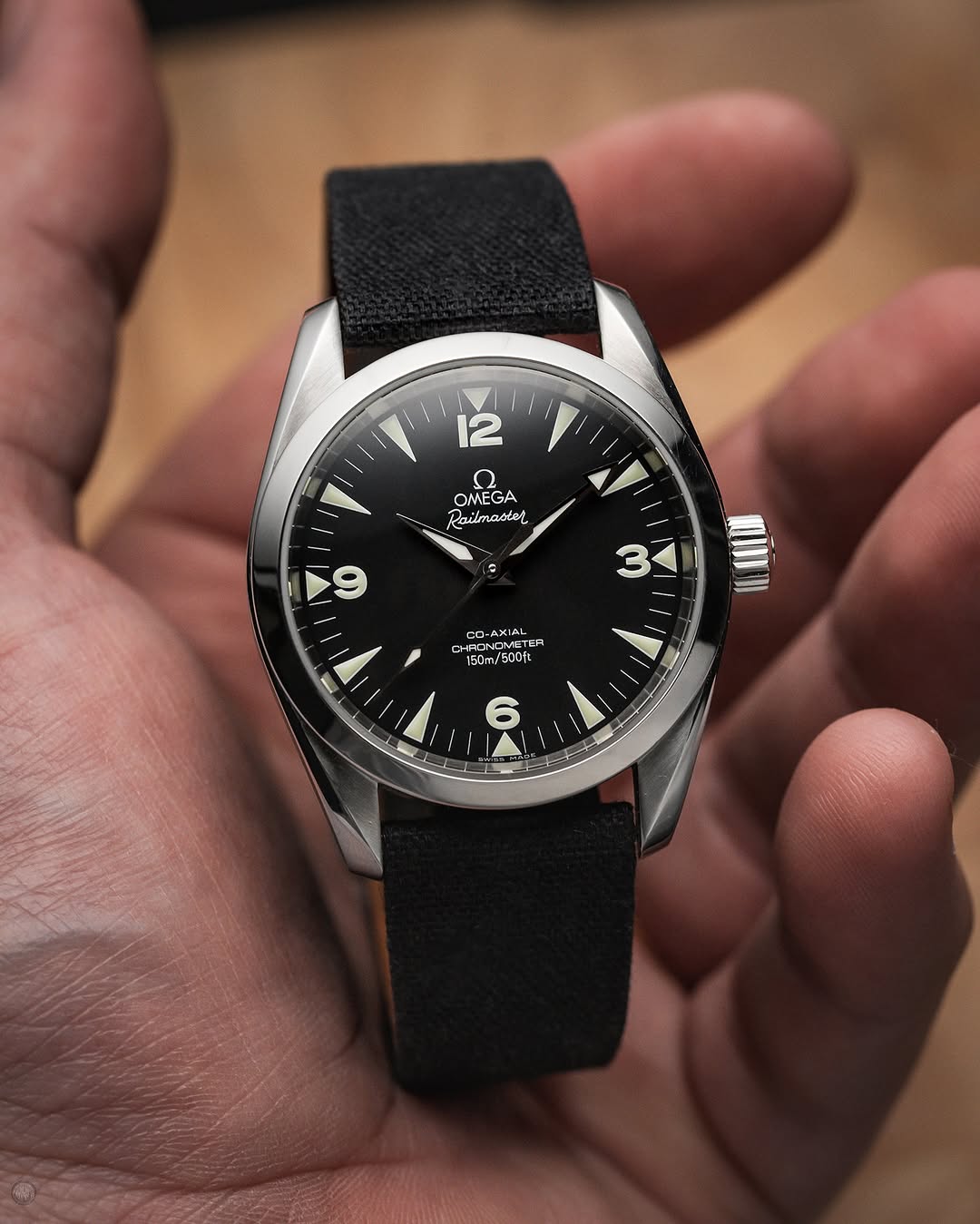 This omega rail master at 36mm is a gem seen here fitted on the RSM basic fine canvas strap in Black Coal color. The watch and strap rests on a palm that shows the small watch with inverted lugs and arrow hands.